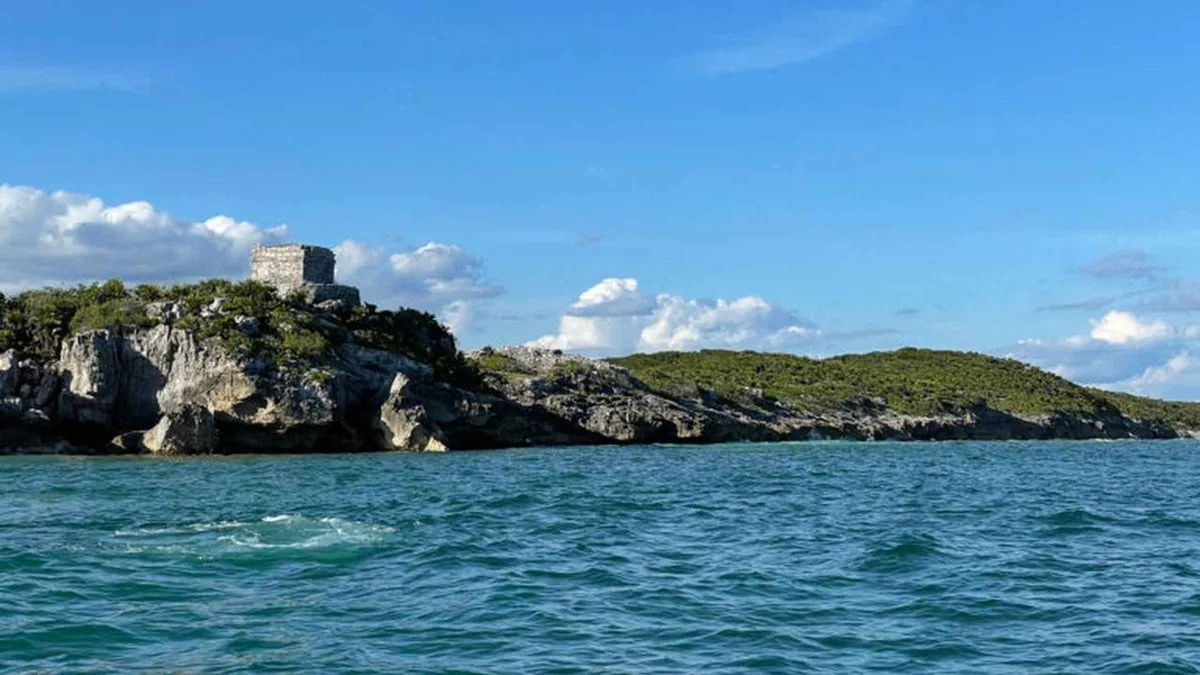 Boat passing below the cliff-top temple on a Tulum ruins by boat and turtle snorkel tour, Tulum Mexico